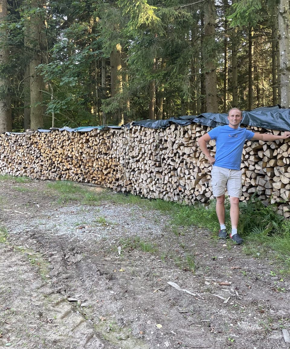 Mann steht vor grossem Brennholzstapel im Wald – Forstservice-Krammer